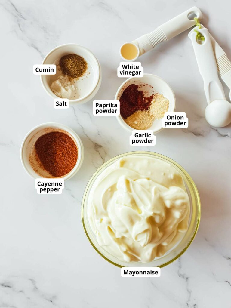 Ingredients for spicy mayonnaise arranged on a marble surface with measuring spoons.