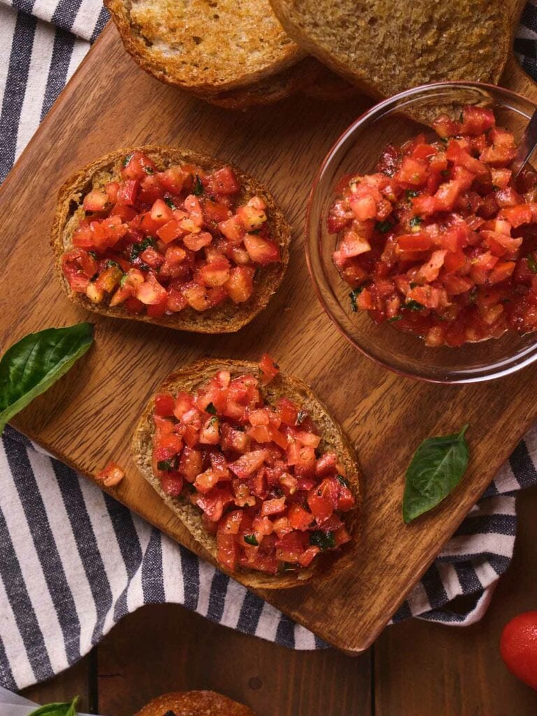 Sliced bread topped with diced tomatoes and herbs on a wooden board.