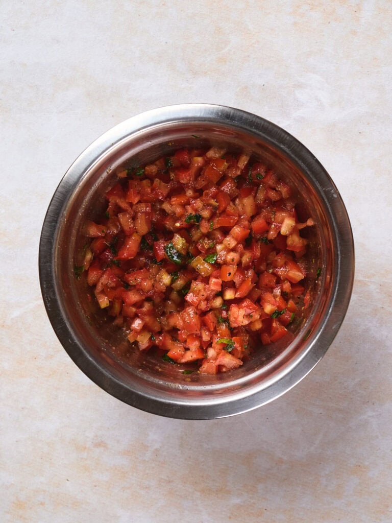 A stainless steel bowl containing freshly chopped tomatoes and cilantro mixed with spices.