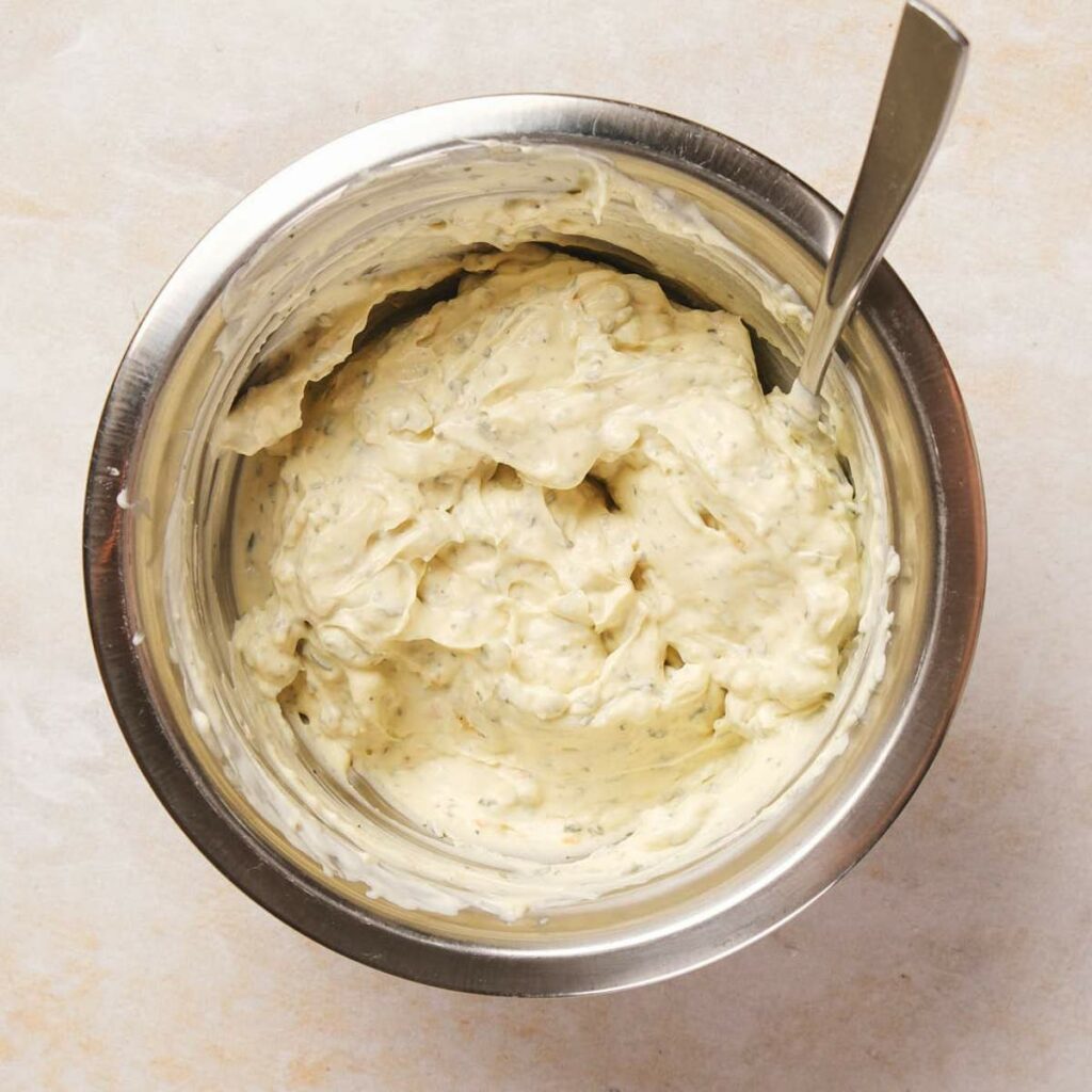 A stainless steel bowl filled with creamy, herb-infused spread.