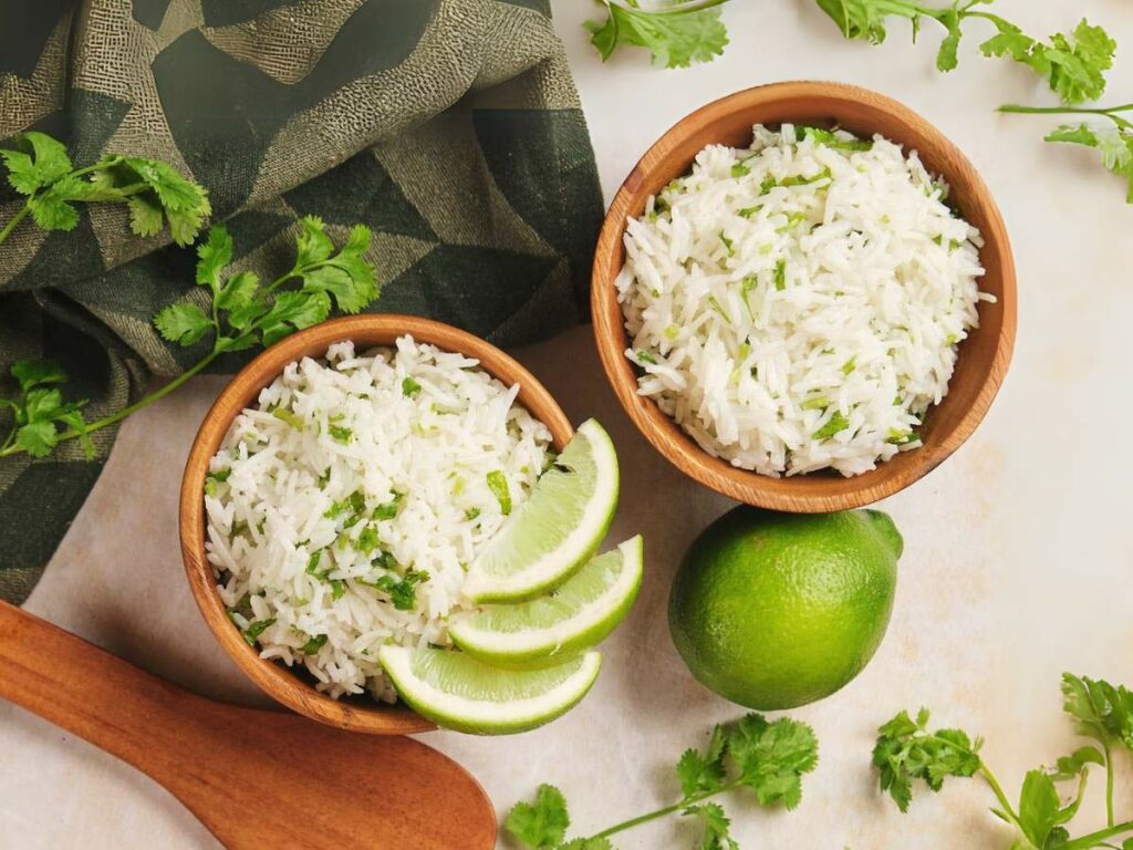 Two wooden bowls of cilantro lime rice garnished with cilantro, accompanied by lime wedges.