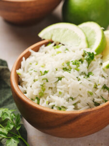 A wooden bowl filled with cilantro lime rice, topped with slices of lime, and garnished with fresh cilantro.