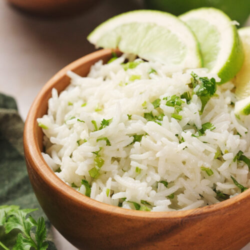 A wooden bowl filled with cilantro lime rice, topped with slices of lime, and garnished with fresh cilantro.