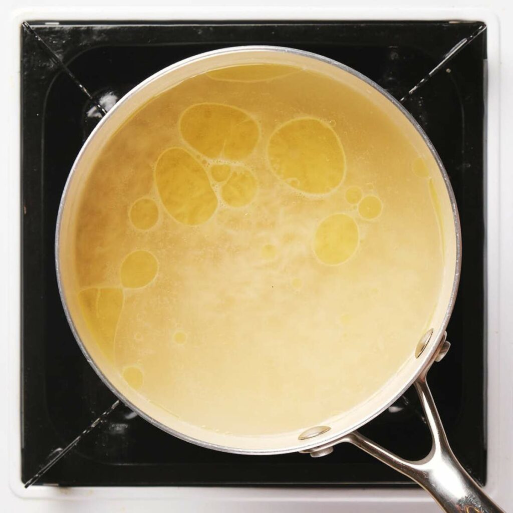 A pot of boiling water with oil droplets on the surface sits on a black stove.