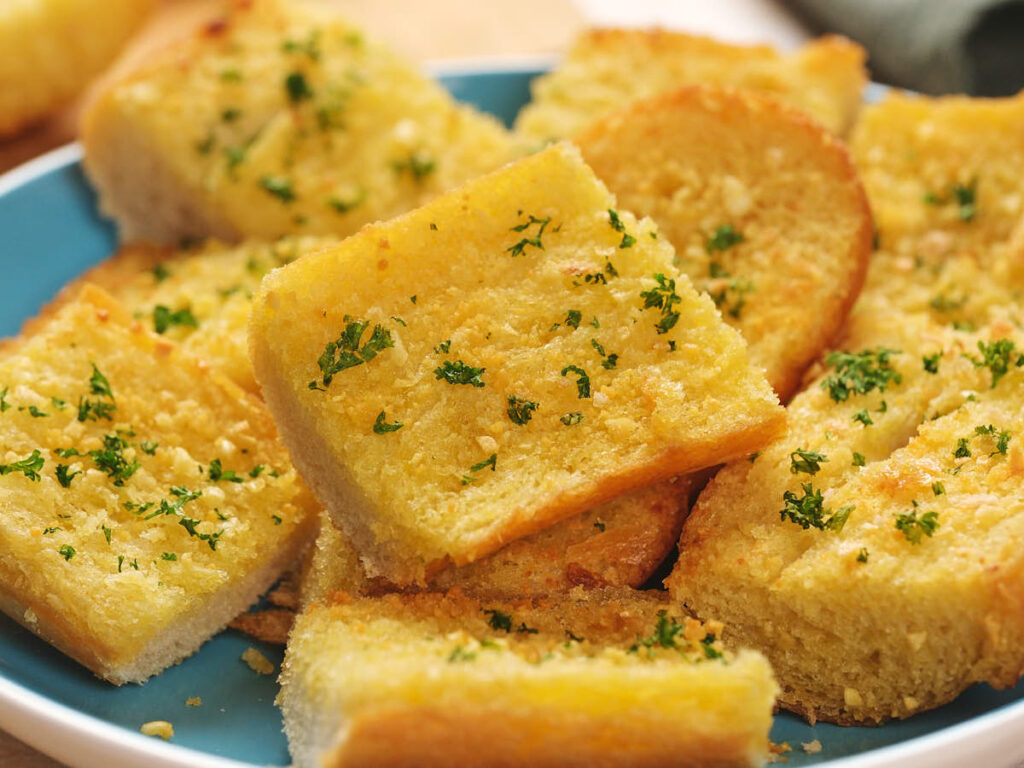 Slices of garlic bread garnished with chopped parsley on a blue plate.