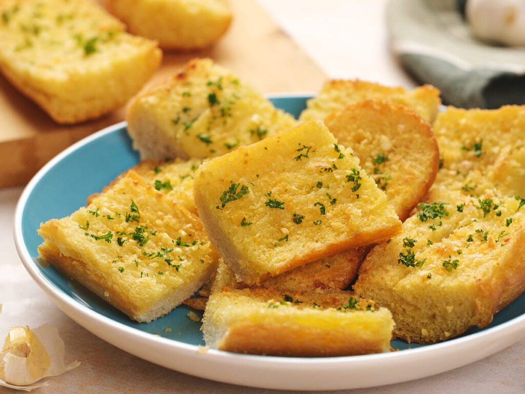 A plate of sliced garlic bread topped with parsley on a blue plate.