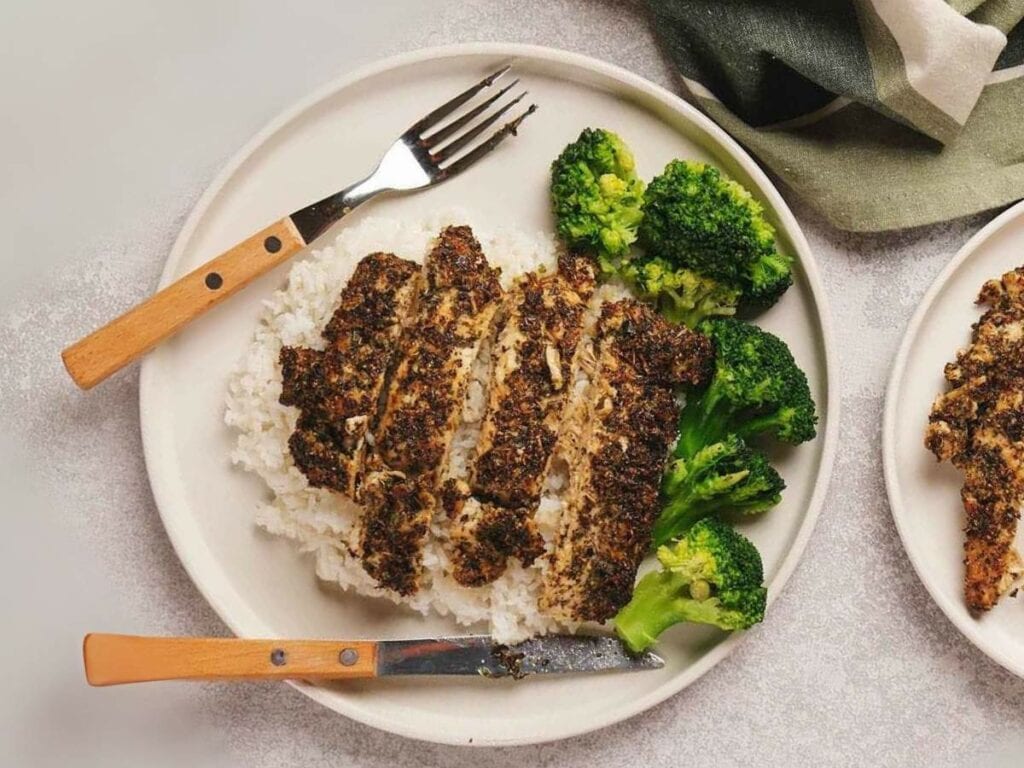 A plate with sliced herb-crusted chicken, white rice, and broccoli.