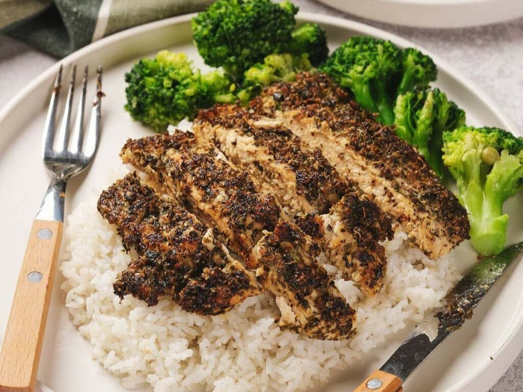 Grilled seasoned chicken sliced over white rice, served with broccoli on a plate.