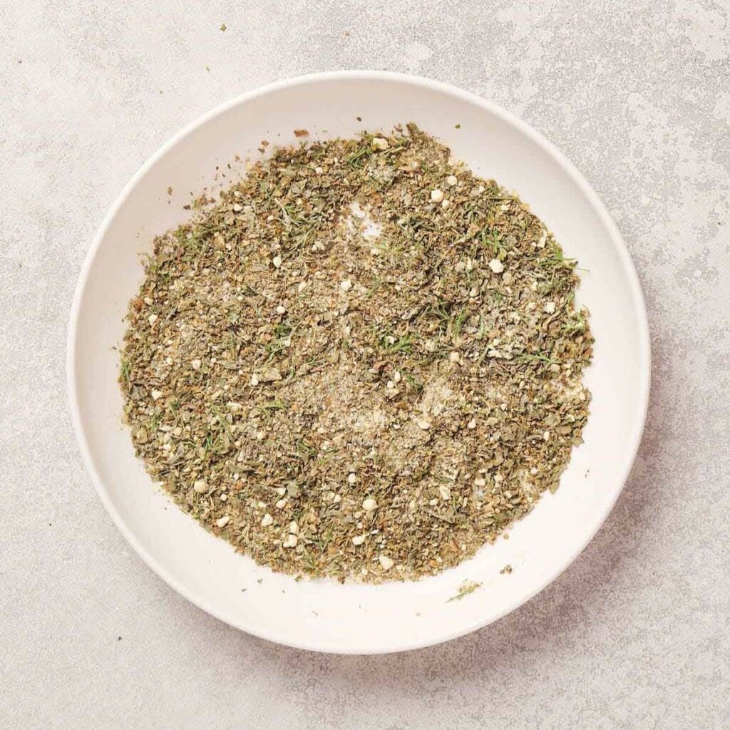 White bowl filled with mixed dry herbs and spices on a light gray surface.