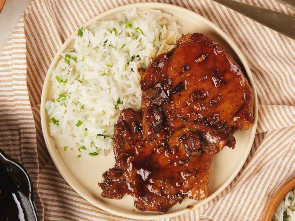 Plate with honey glazed chicken pieces and a serving of herbed rice on a striped cloth background.