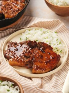 Plate with honey glazed pork chops and white rice, set on a striped cloth.