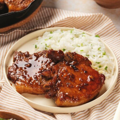 Plate with honey glazed pork chops and white rice, set on a striped cloth.