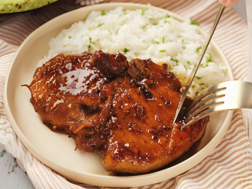 Plate with honey glazed chicken thighs and white rice, fork cutting into the chicken.