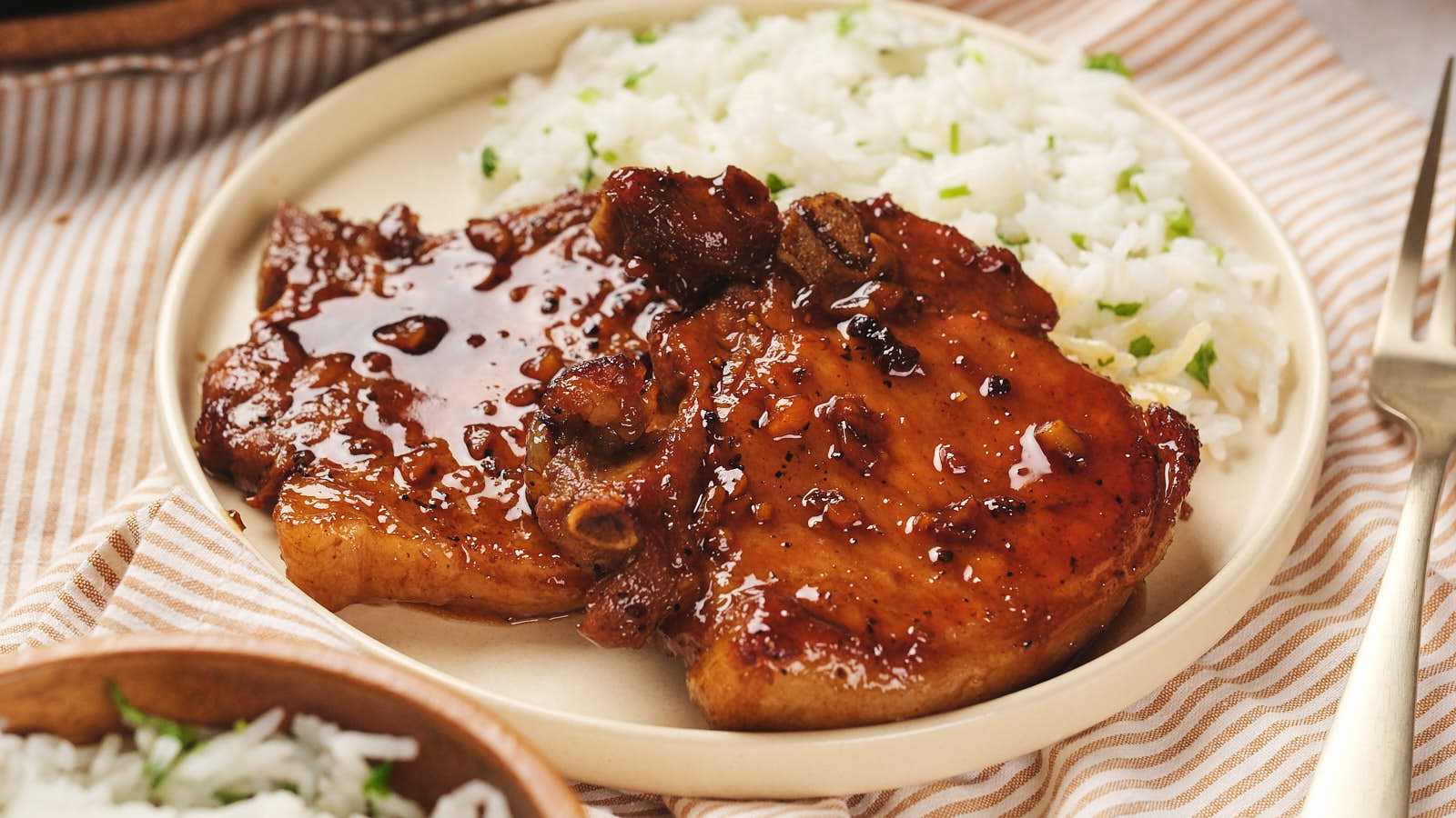 Plate of honey glazed pork chops with a side of white rice on a striped tablecloth.