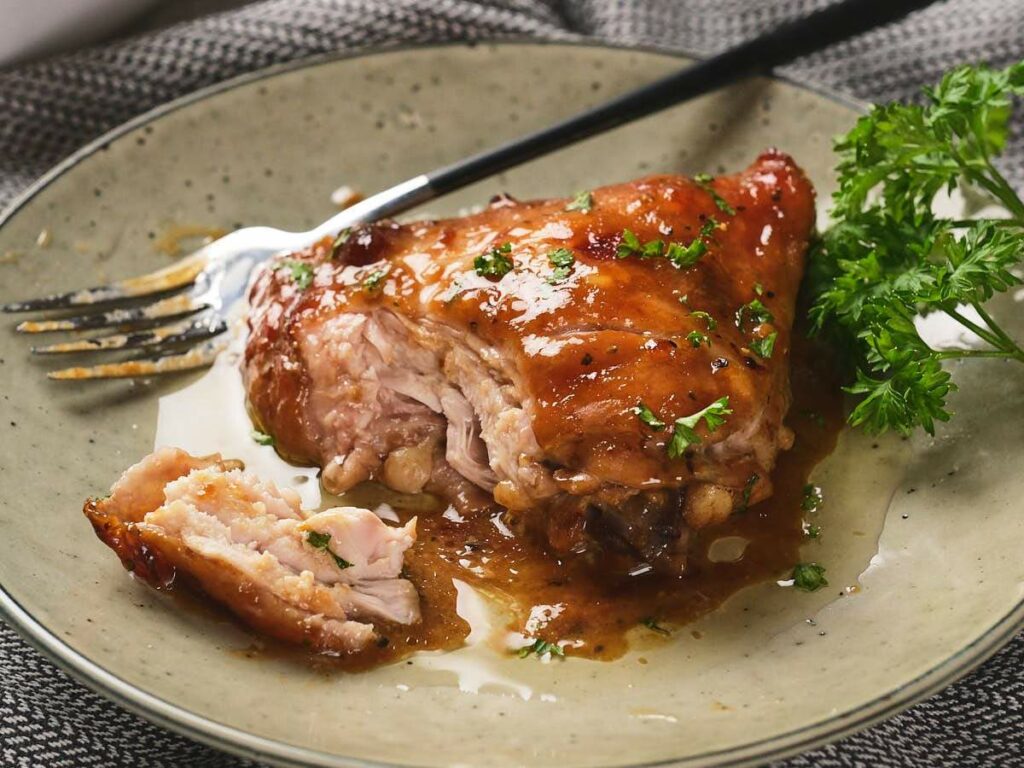 Cooked chicken with apricot sauce and parsley garnish on a plate.