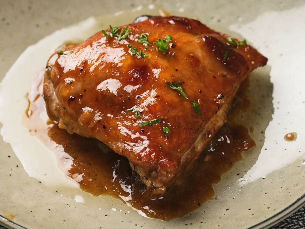 A glazed piece of apricot chicken garnished with chopped herbs on a plate.