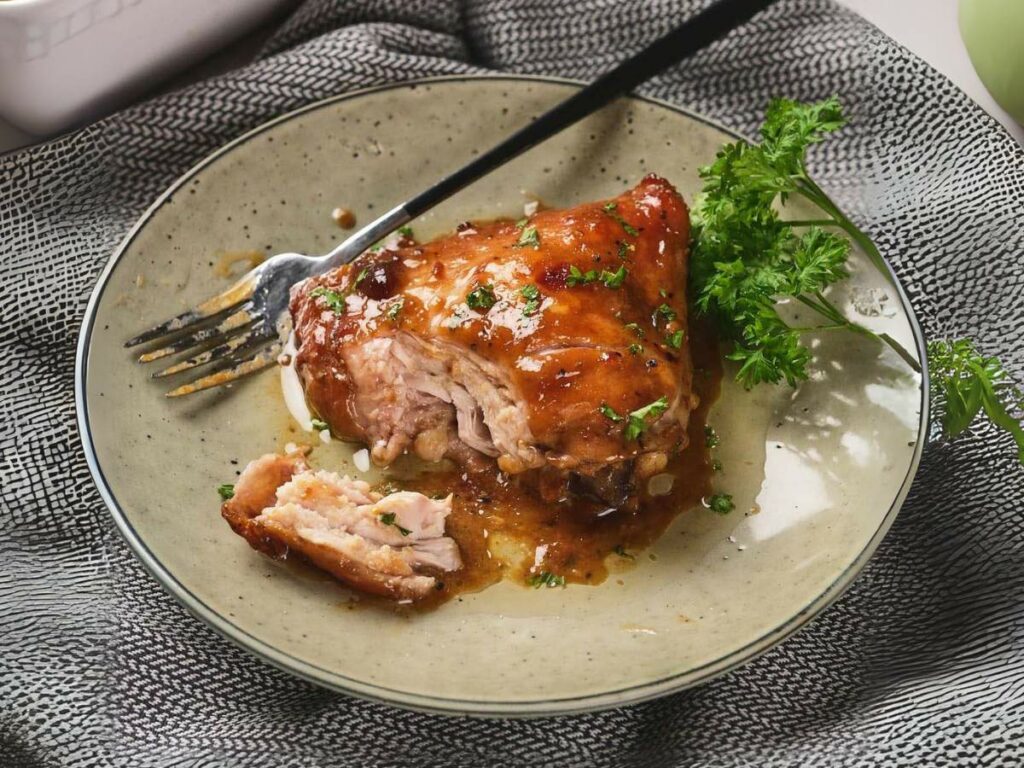 A piece of apricot glazed chicken on a plate with a fork, garnished with parsley.