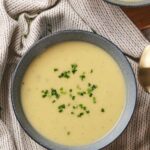 A bowl of potato and leek soup garnished with chopped green herbs on a striped cloth.