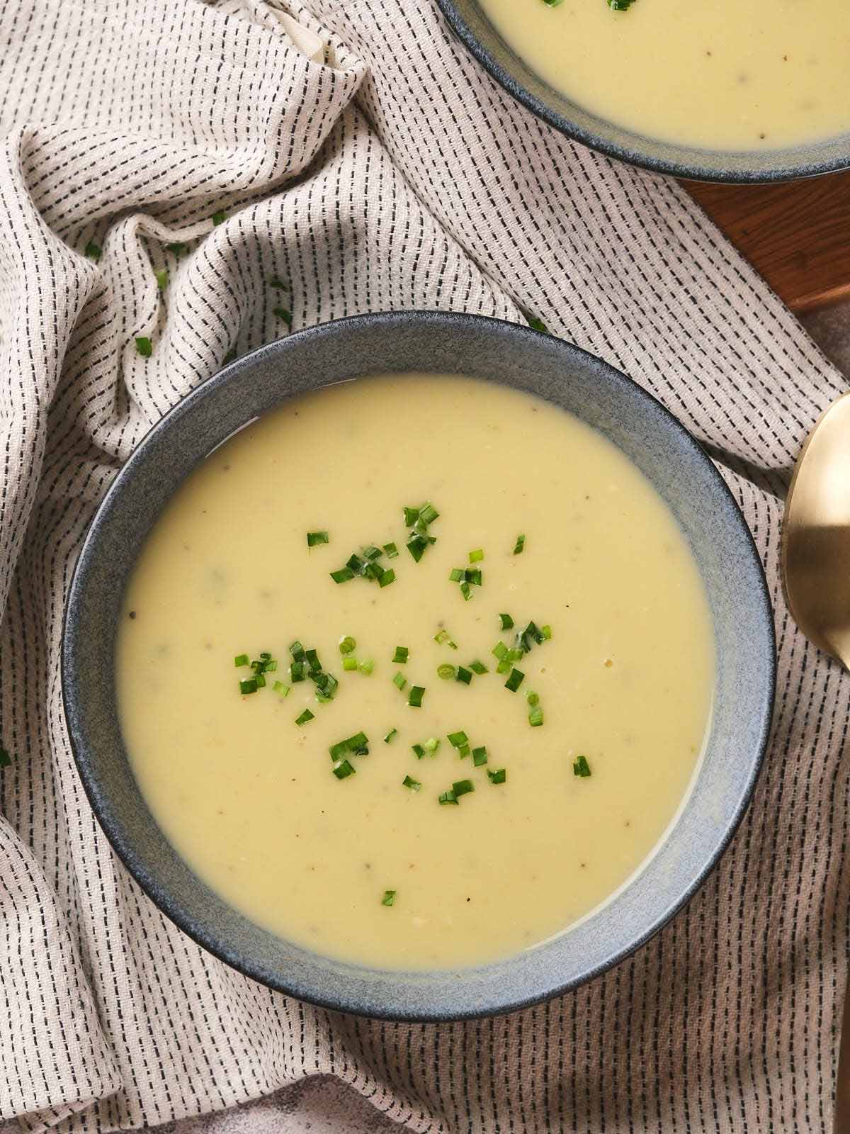 A bowl of potato and leek soup garnished with chopped green herbs on a striped cloth.