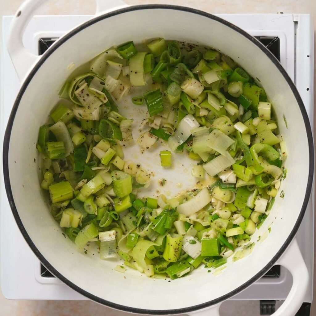 Chopped green onions sautéing in a white pot on a stovetop.