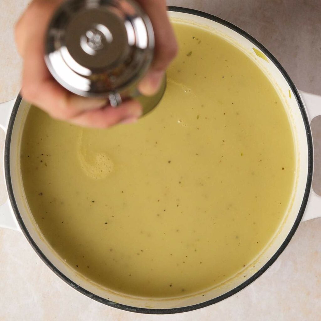 Hand seasoning a pot of creamy soup with black pepper.