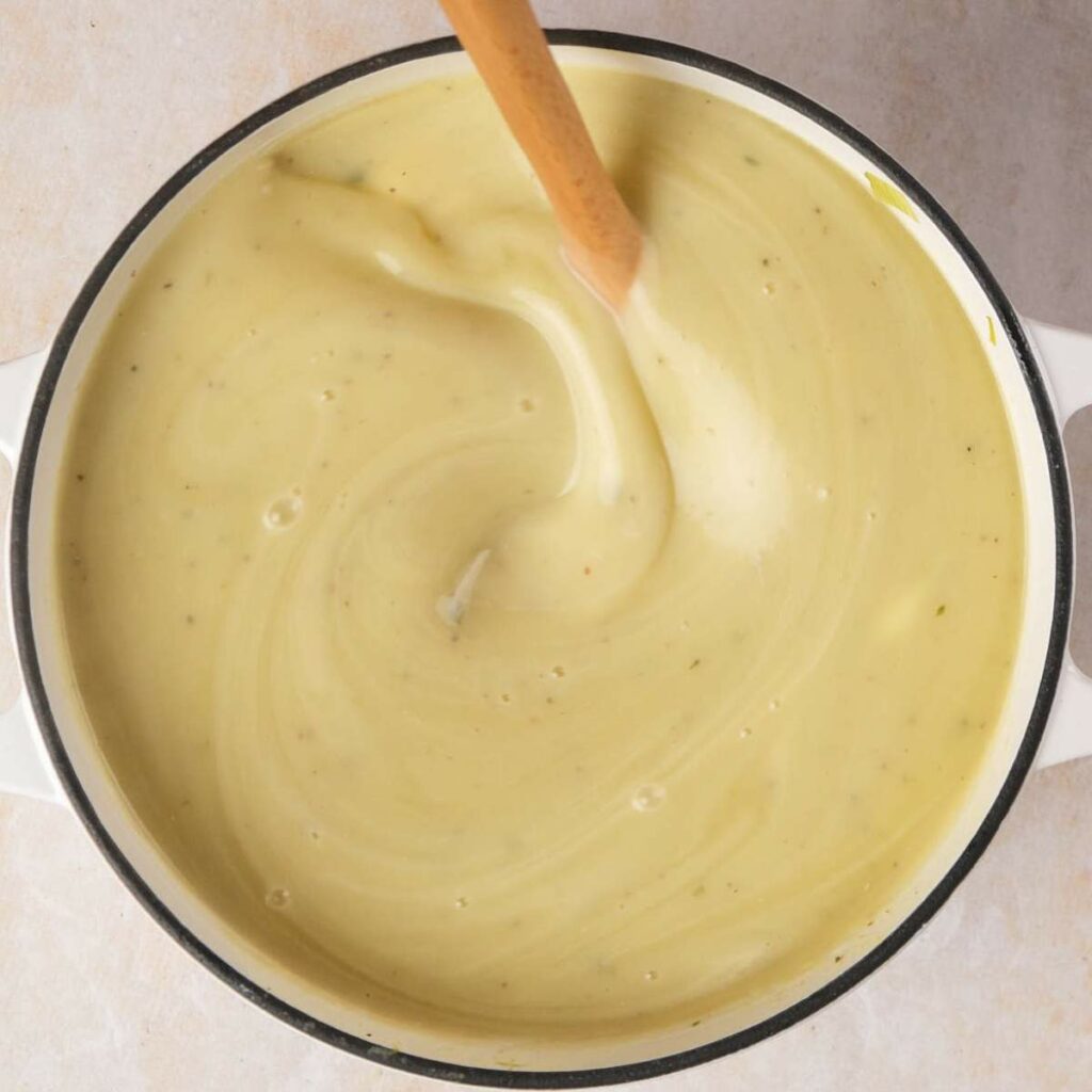 A pot of creamy yellow soup being stirred with a wooden spoon.