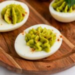 Avocado deviled eggs served on a wooden tray.