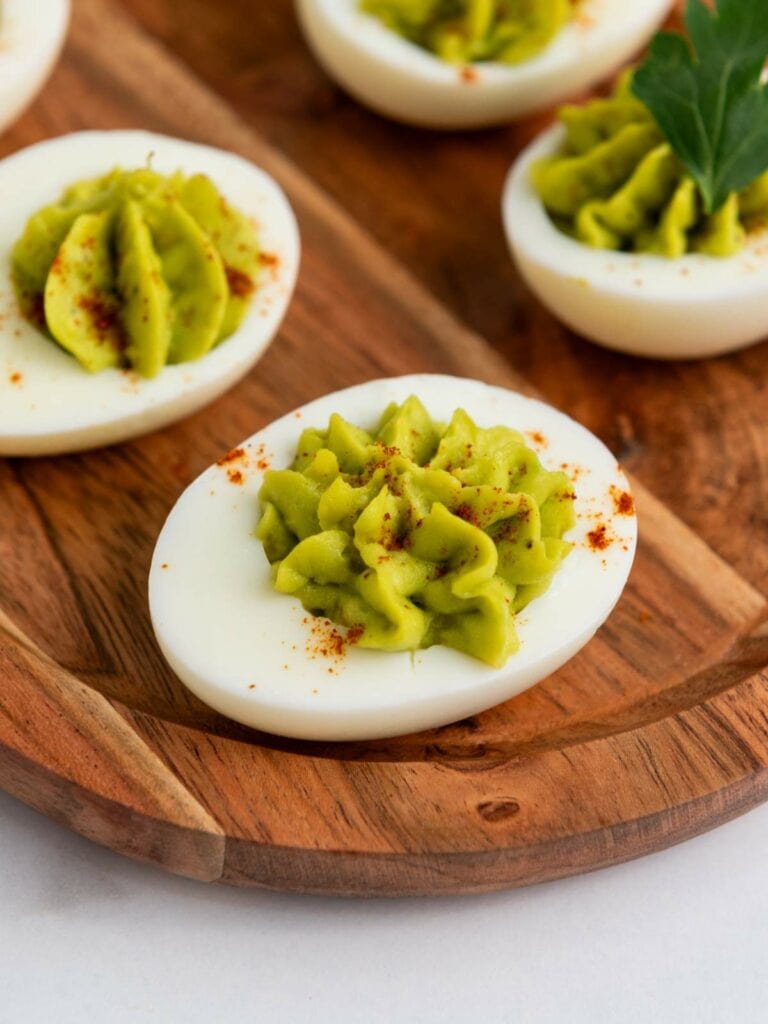 Avocado deviled eggs served on a wooden tray.