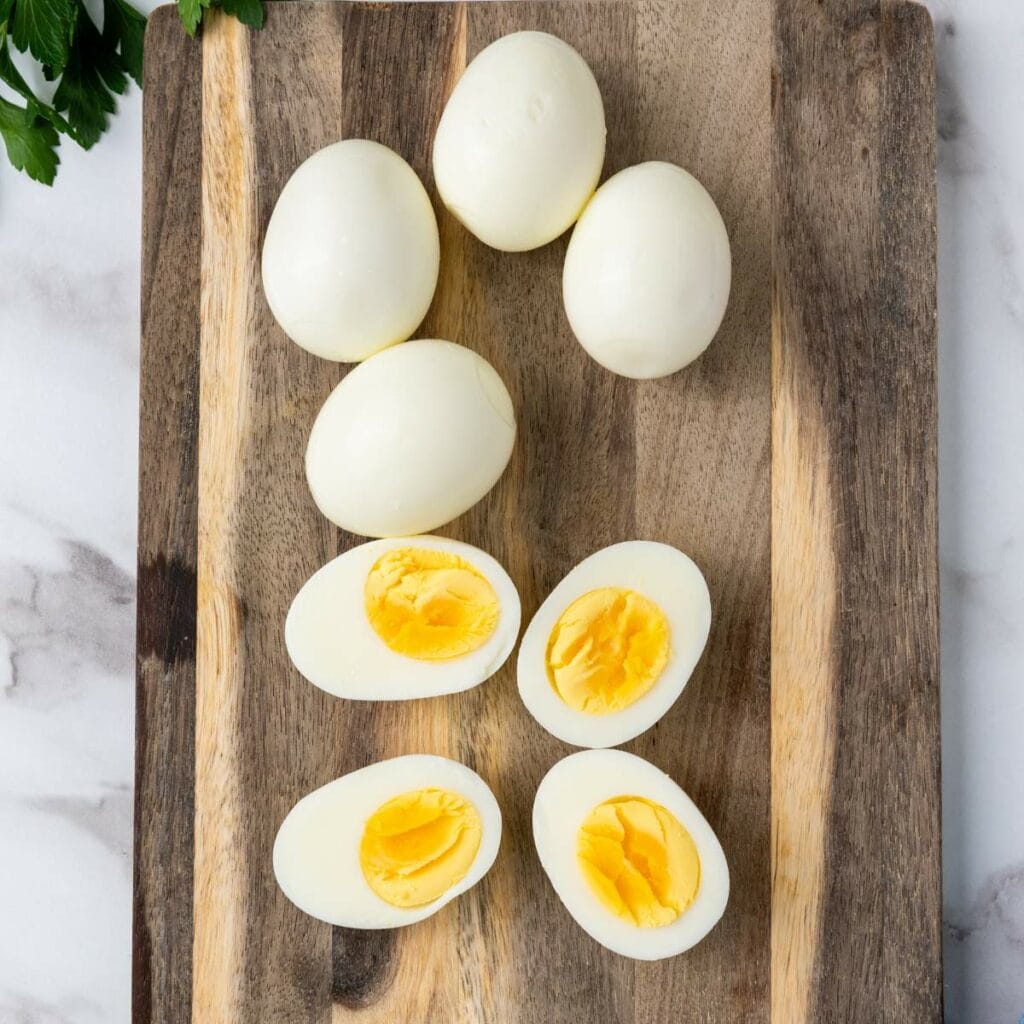 Peeled hard-boiled eggs, some whole and some halved, on a wooden cutting board.