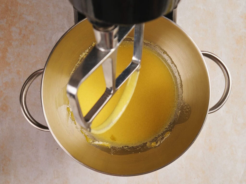 Mixer with paddle attachment blending melted butter in a metal bowl.