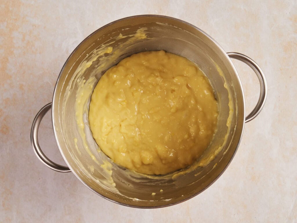 A stainless steel bowl containing smooth, thick yellow batter on a light marbled surface.