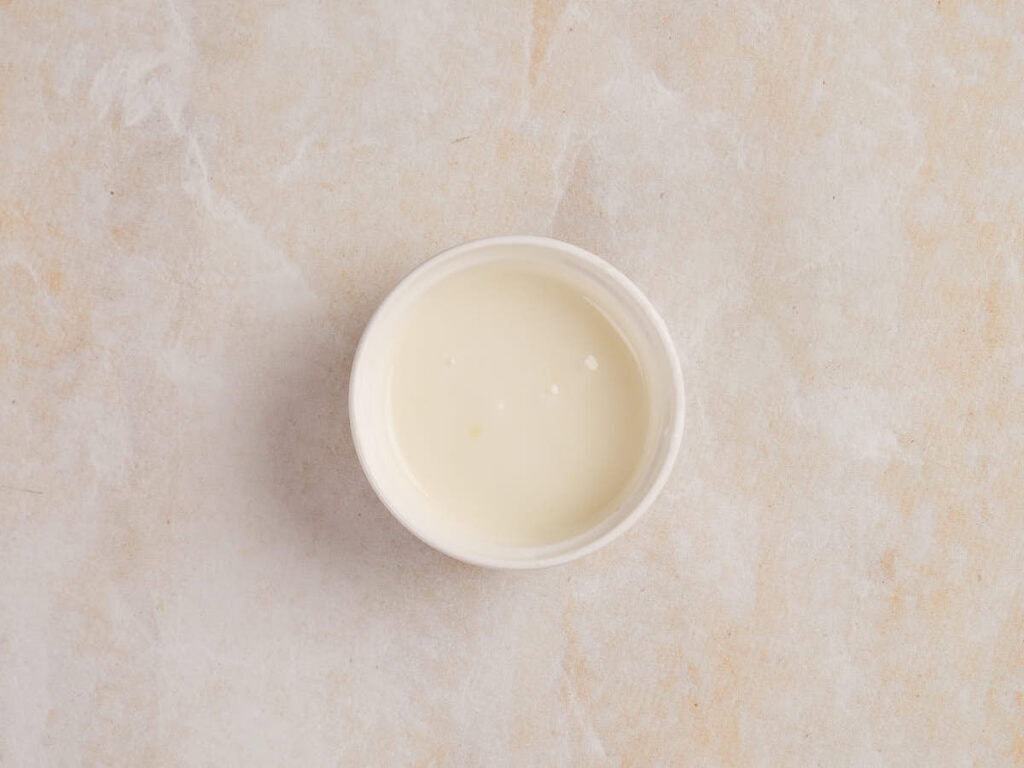 Small white bowl filled with a creamy white liquid on a light marbled surface.