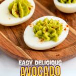 A wooden platter with deviled eggs topped with avocado filling and sprinkled with paprika, labeled "Easy Delicious Avocado Deviled Eggs.