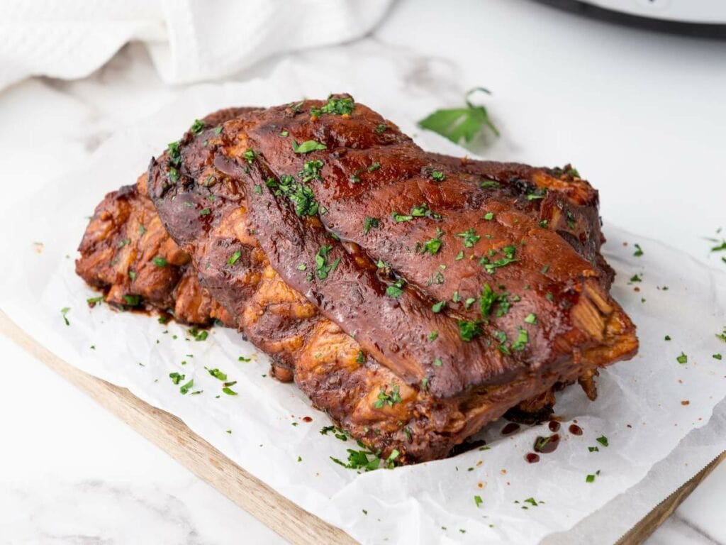 Baby back ribs garnished with chopped herbs, resting on parchment paper.
