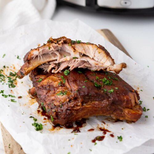 Baby back ribs garnished with chopped herbs are placed on parchment paper.