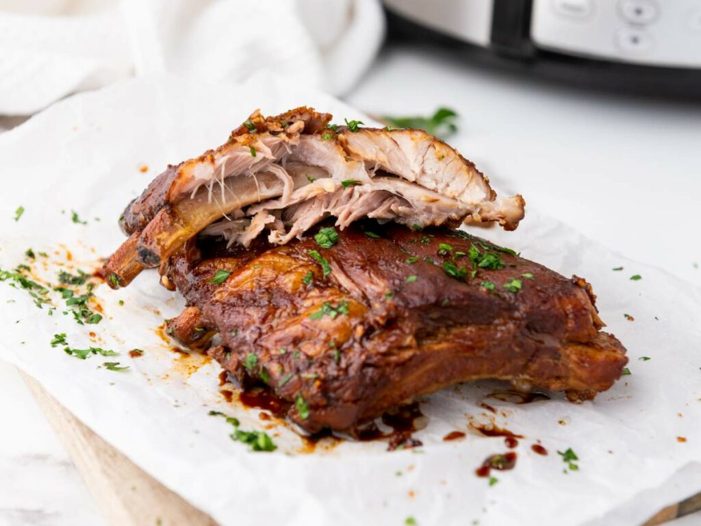 Cooked baby back ribs with a glazed, browned exterior are garnished with chopped herbs.