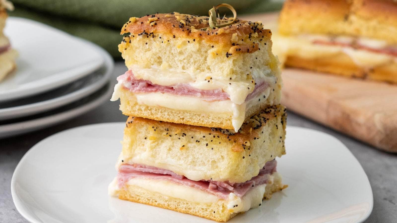 Ham and cheese sliders with poppy seeds and garlic topping on a wooden board.