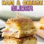Two baked ham and cheese sliders with poppy seeds on top are stacked on a plate, held together with a toothpick.