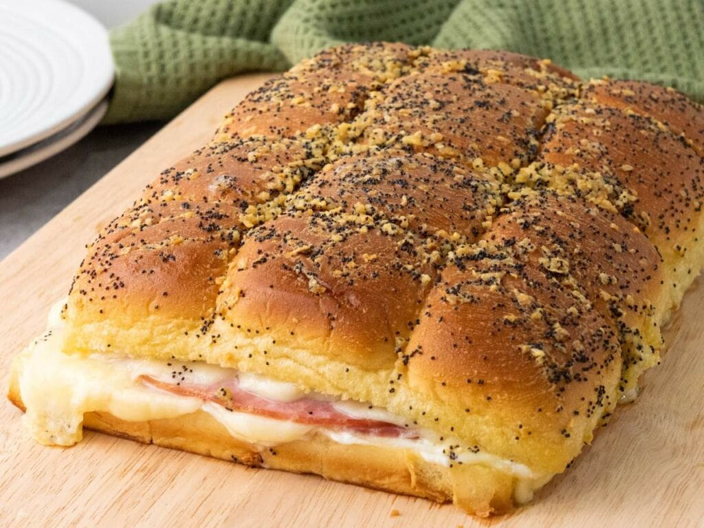 A sandwich made from a large loaf filled with melted cheese and ham, topped with poppy seeds.