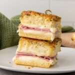 Two stacked ham and cheese sliders made with poppy seed-topped bread on a white plate.