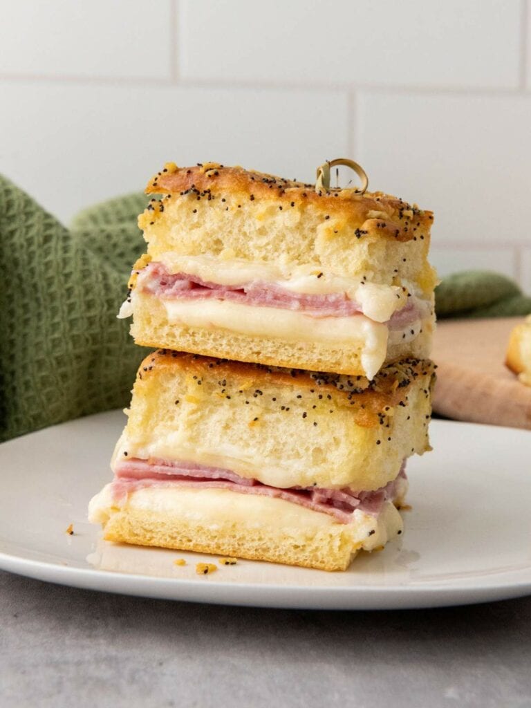 Two stacked ham and cheese sliders made with poppy seed-topped bread on a white plate.