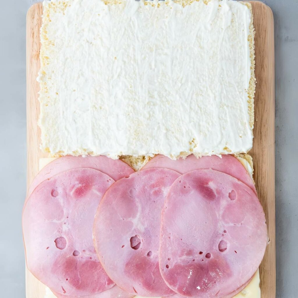Open sandwich with layers of mayonnaise, cheese, and ham on a wooden board.
