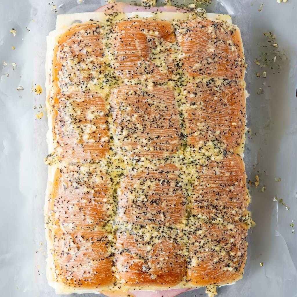 Baked sliders with poppy seed topping on a parchment-lined surface.