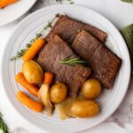 A white plate with slices of cooked rump roast, baby carrots, small potatoes, onions, and a sprig of rosemary.
