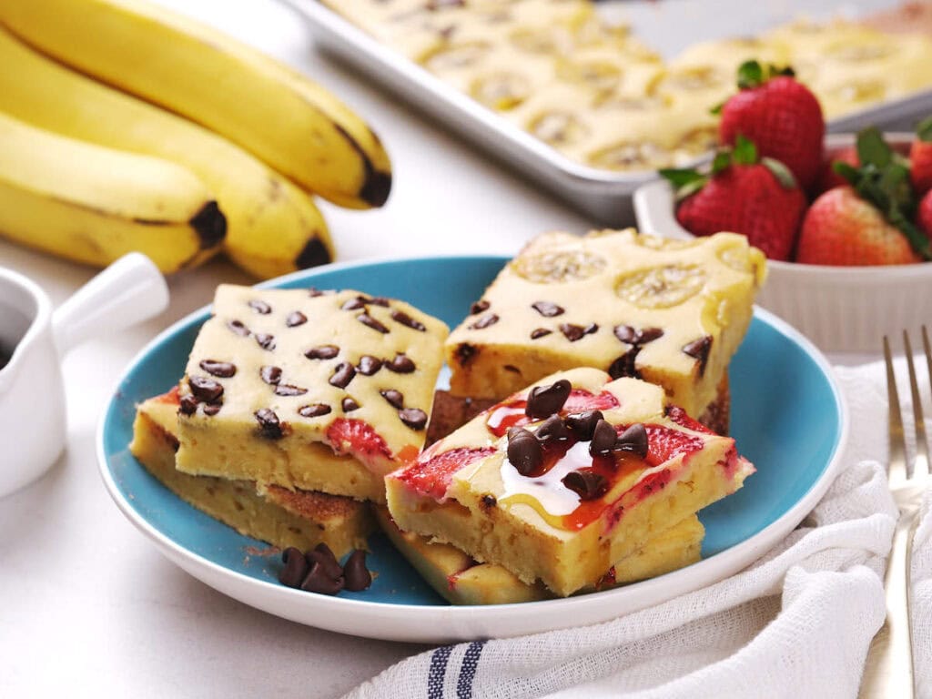 A plate with three pieces of sheet pan pancakes topped with chocolate chips and strawberries.