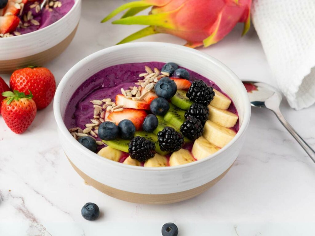 A smoothie bowl topped with banana slices, blackberries, blueberries, kiwi, strawberries, and sunflower seeds.