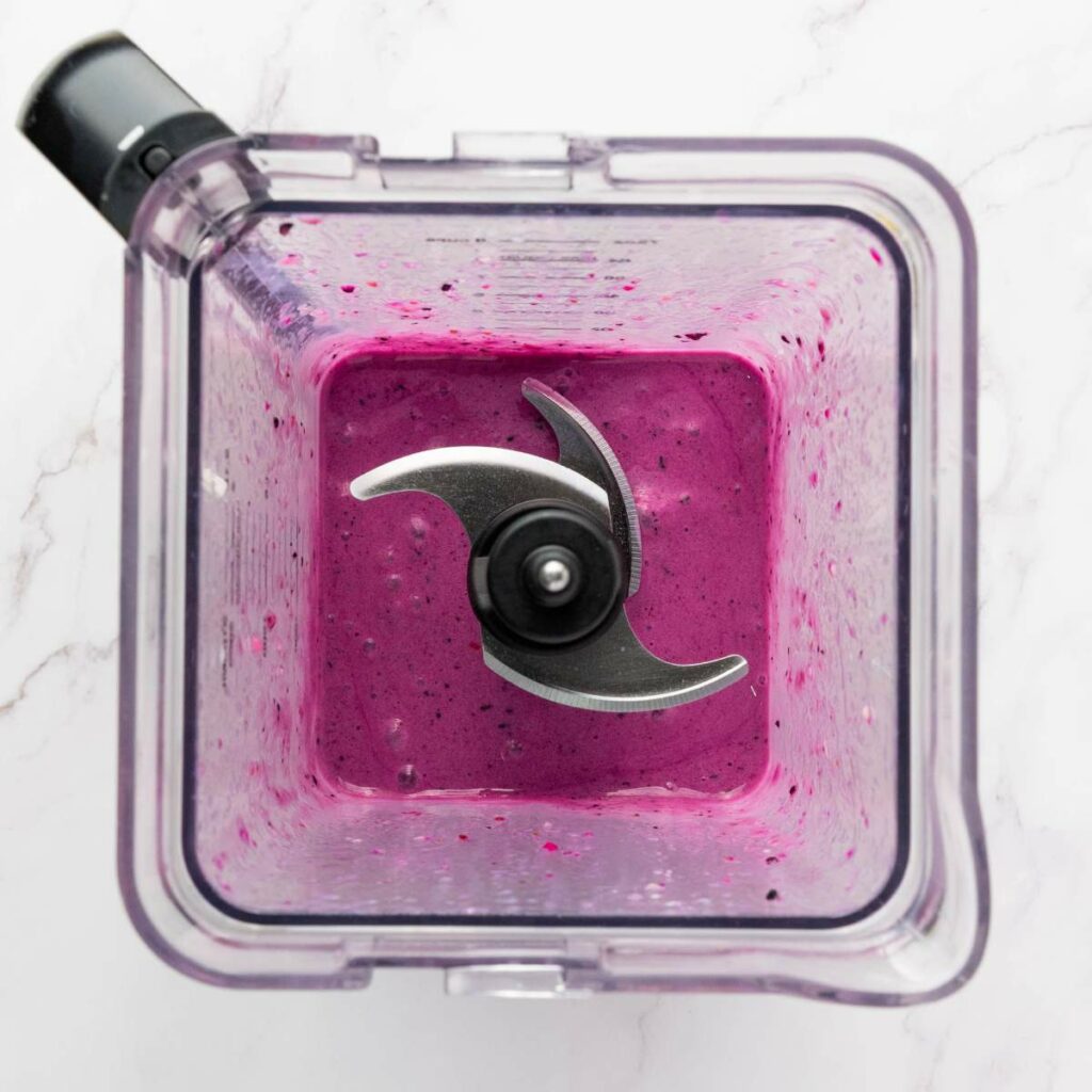 Overhead view of a blender containing a thick, purple smoothie mixture with visible blade.