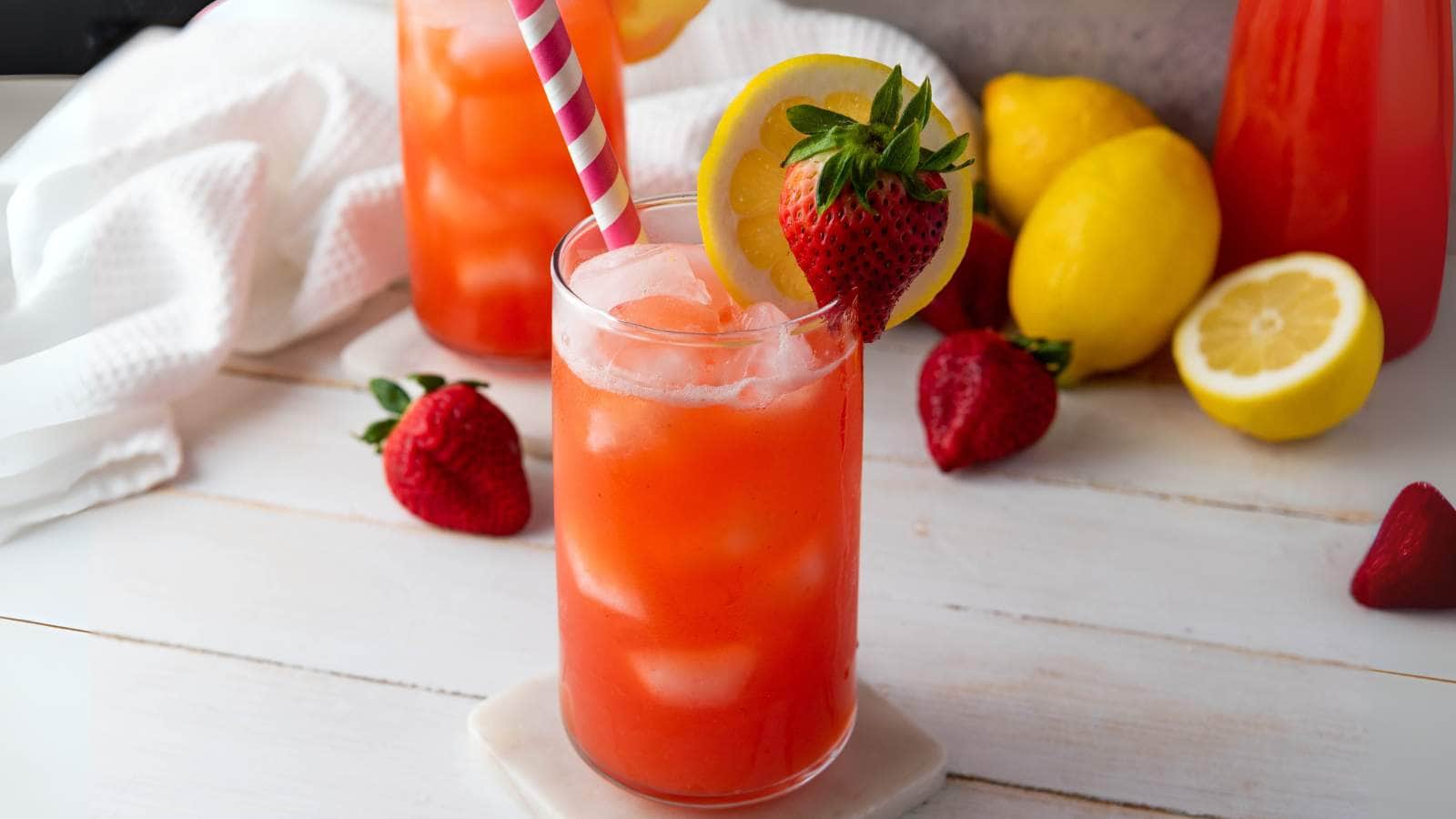 A glass of strawberry lemonade with ice, adorned with a lemon slice and a strawberry.
