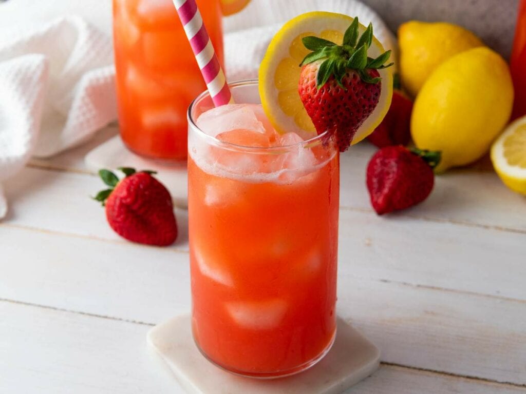 A refreshing strawberry lemonade with ice, garnished with a lemon slice and whole strawberry.