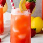 A glass of strawberry lemonade with ice, garnished with a slice of lemon and a whole strawberry.